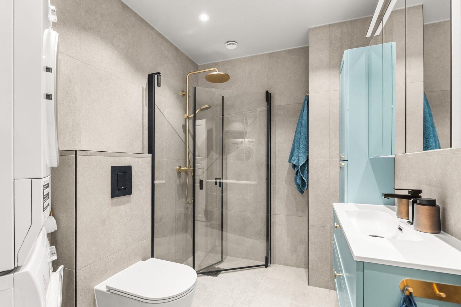 Badet er utstyrt med dusjhjørne med glassveger, servantseksjon med skuffer og komposittvask, høyskap, speil med lys, vegghengt wc og opplegg for vaskemaskin. Galleribilde