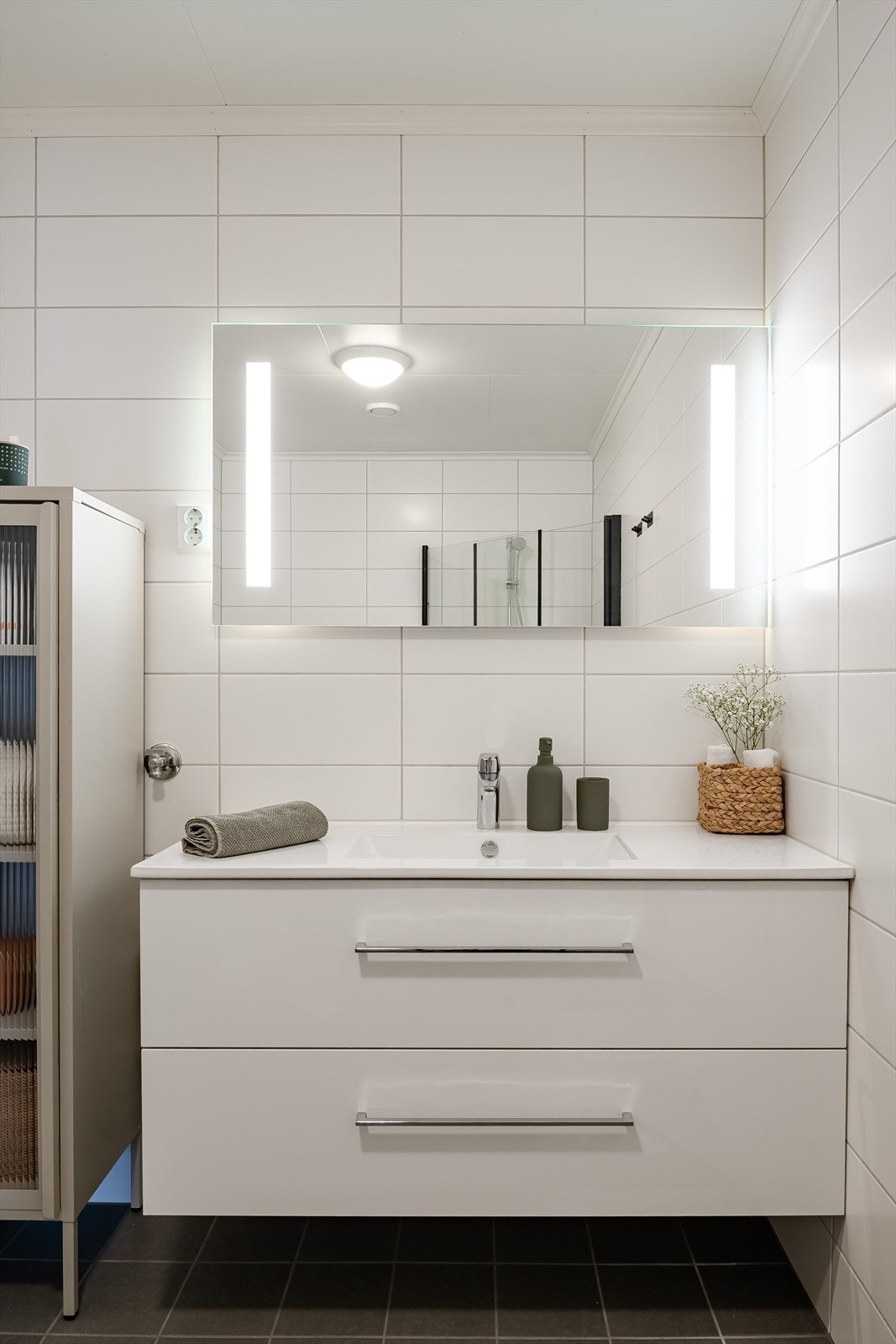 Moderne baderomsinnredning med skuffer og heldekkende servant, speil med integrert belysning over. Galleribilde