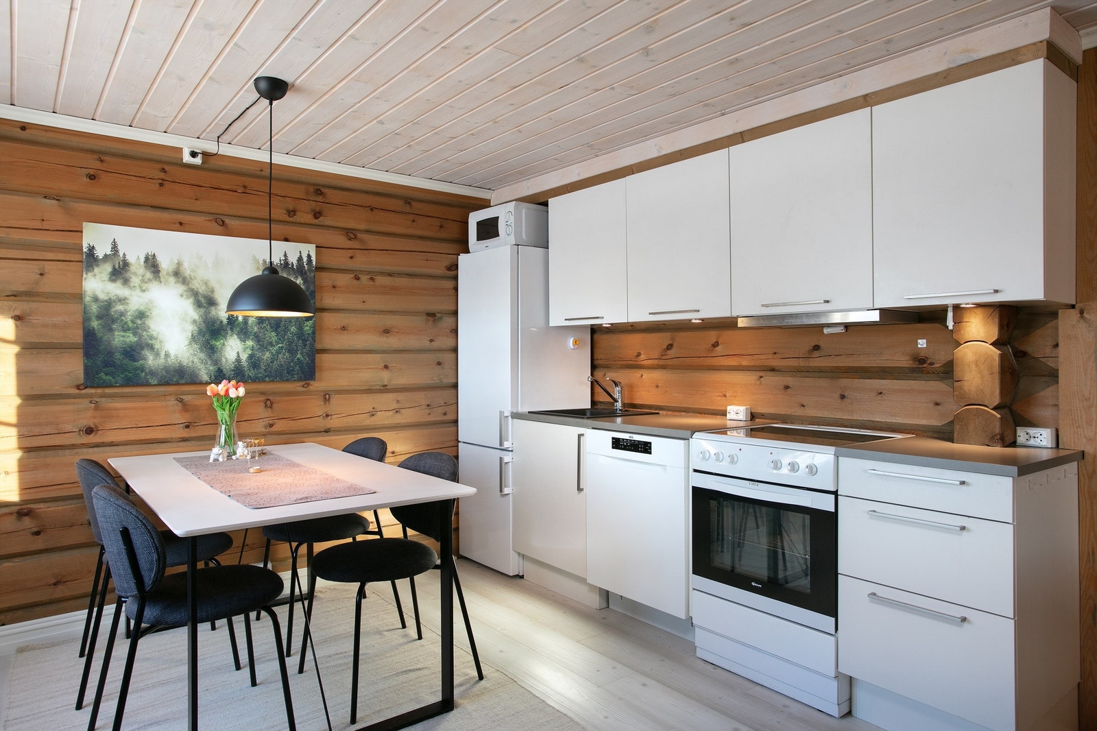 Hvit kjøkkeninnredning med glatte fronter og benkeplate av laminat. Det er kjøl/fryseskap, oppvaskmaskin, komfyr, vannstoppsystem og komfyrvakt. Kjøkkenventilator med avtrekk ut. Galleribilde