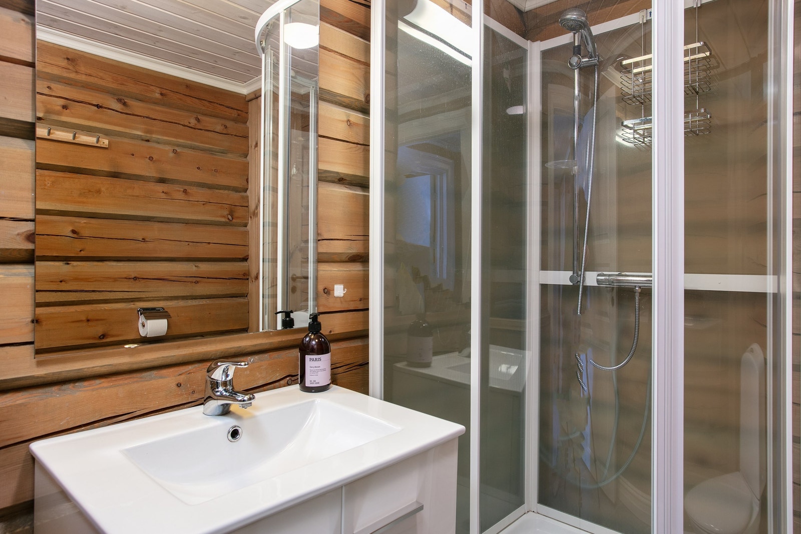 Baderomsinnredning med ovenpåliggende servant med ett-greps armatur. Speil over servant. Gulvstående toalett og dusjkabinett. Galleribilde