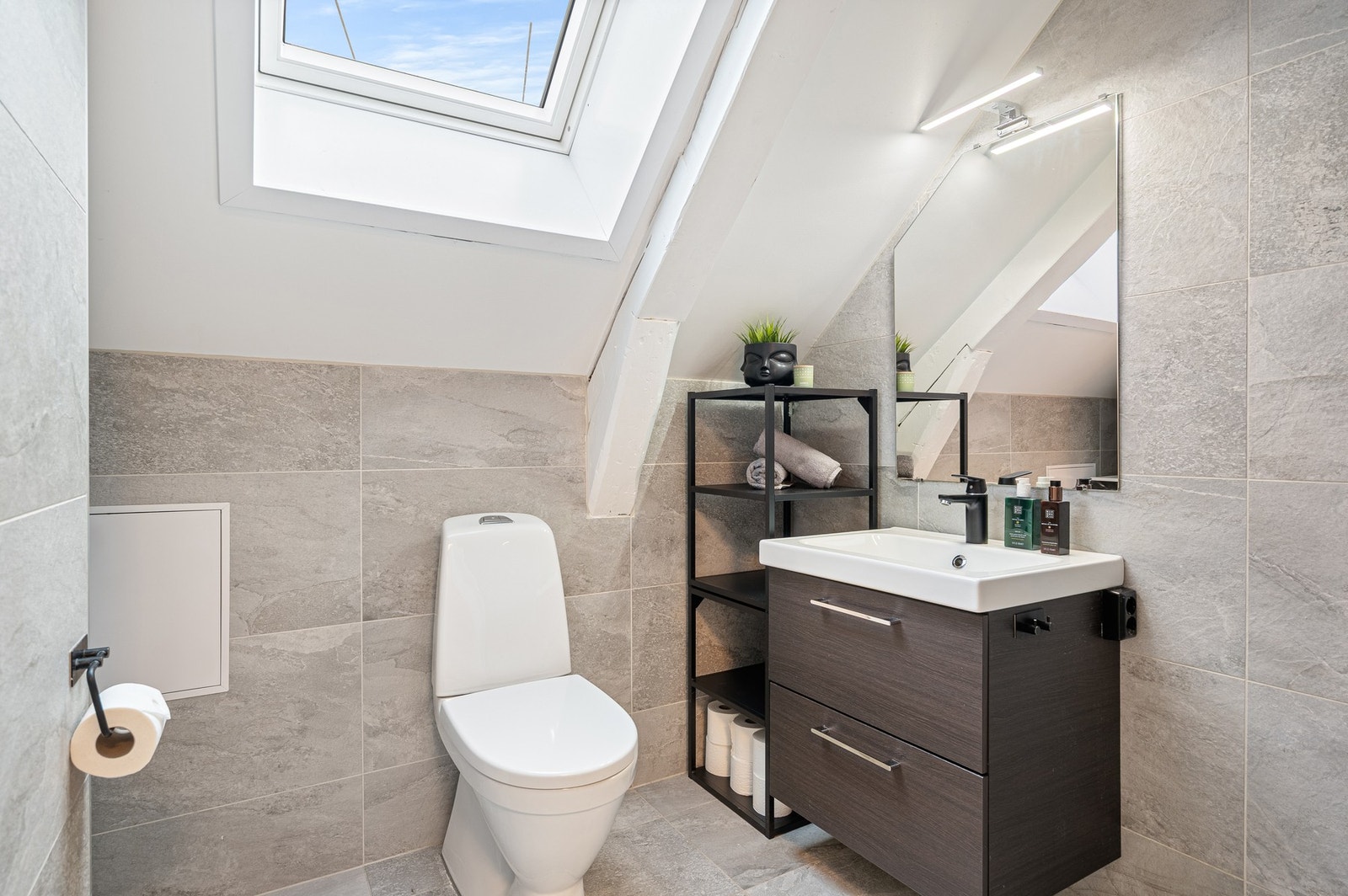 Stilrent bad med flis på overflater og praktisk innredning, med gode oppbevaringsmuligheter. Galleribilde