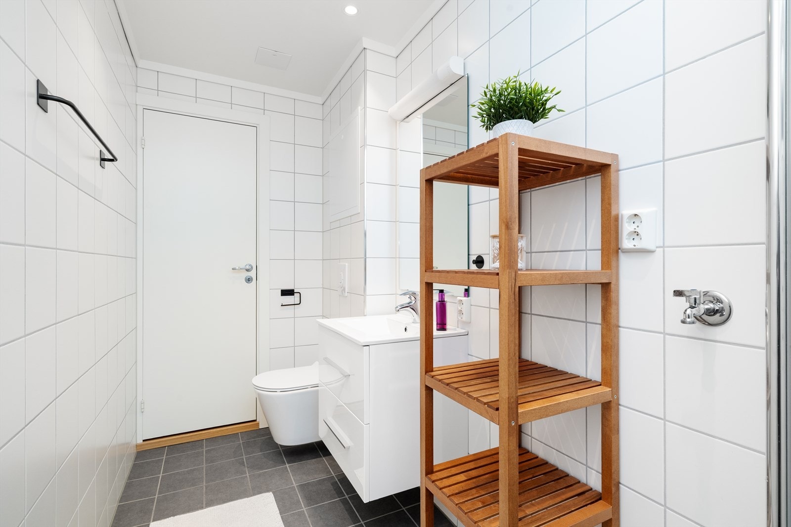 Badet inneholder heldekkende servant med underskap, speil med lys over, dusjhjørne med innfellbar glassdør, vegghengt toalett og opplegg til vaskemaskin Galleribilde