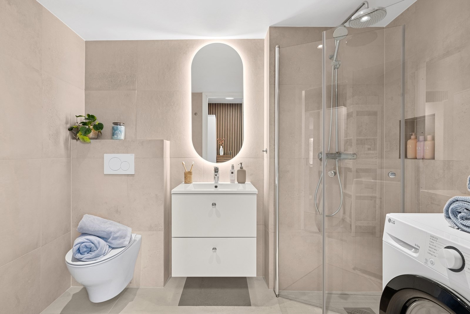 Delikat flislagt bad fra 2024 med vegghengt toalett, dusjhjørne, servant og opplegg for vaskemaskin. Galleribilde