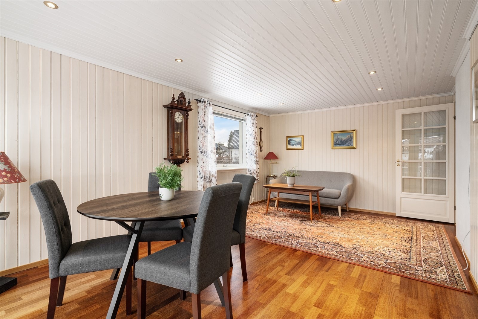 Overflater i stua er parkett på gulv, malt panel på vegger og malt panel med dimbare spotter i tak. Galleribilde