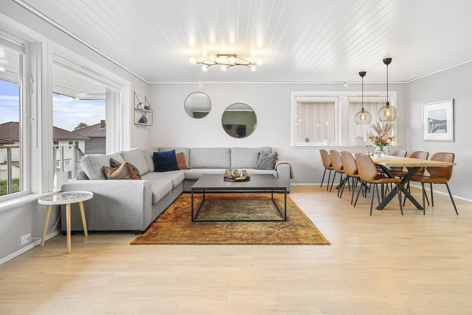 Gulvet har lys parkett, kombinert med vegger malt i lysegrått og en mørk grønnfarge. Stuen er naturlig inndelt i ulike soner, og utenfor kjøkkenet samles familien for hyggelige måltider rundt et langbord. Galleribilde