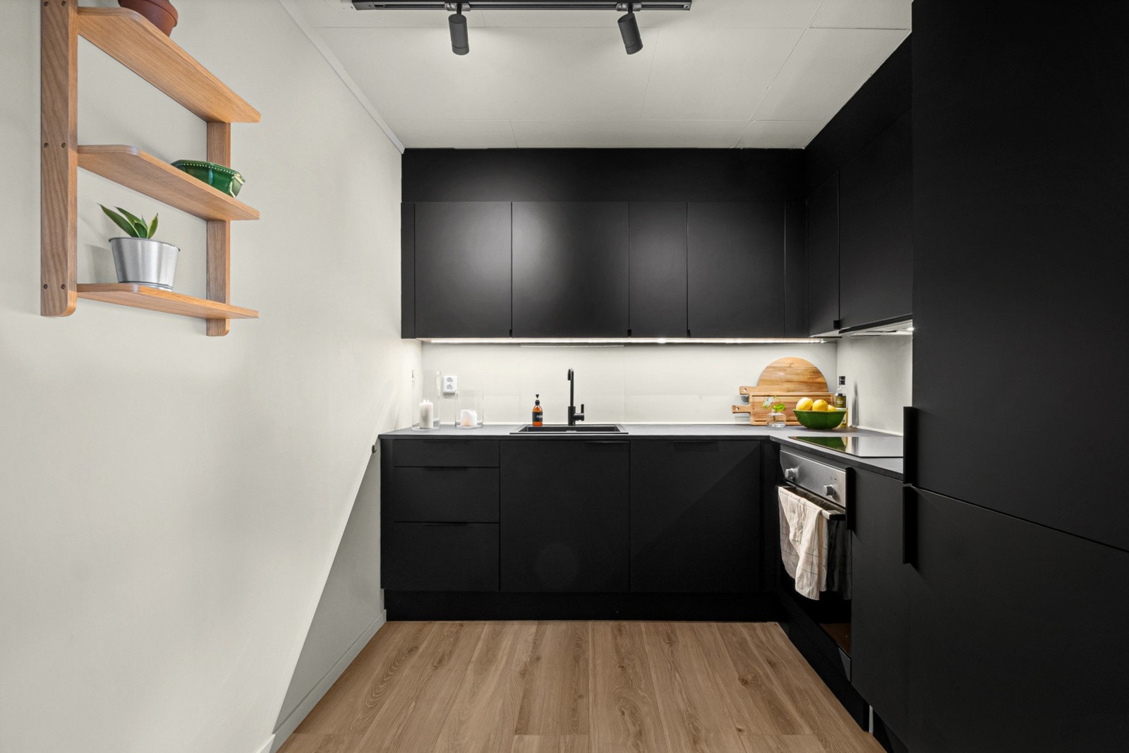 Moderne kjøkkeninnredning med stilrene, sorte slette fronter og godt utnyttet oppbevaringsplass med både benker og overskap. Galleribilde