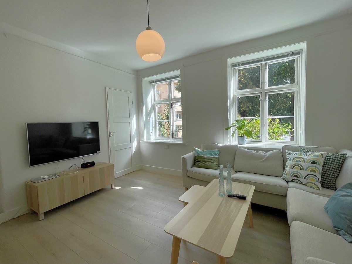 Stue med 2 store vinduer mot trærne på Sofies Plass. Galleribilde