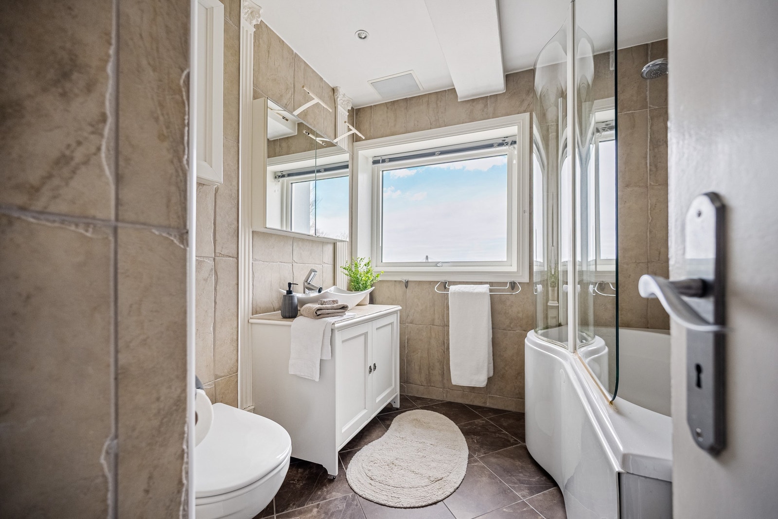 Fint helfliset bad som var rehabilitert i 2008. Det er veggheng toalett, servant med underskap, speilskap på vegg. Varmekabler i gulv.
Badekar og opplegg for vaskemaskin. I tak på bad er det høyttalere. Dagens eier har ikke brukt disse i sin eiertid. Galleribilde