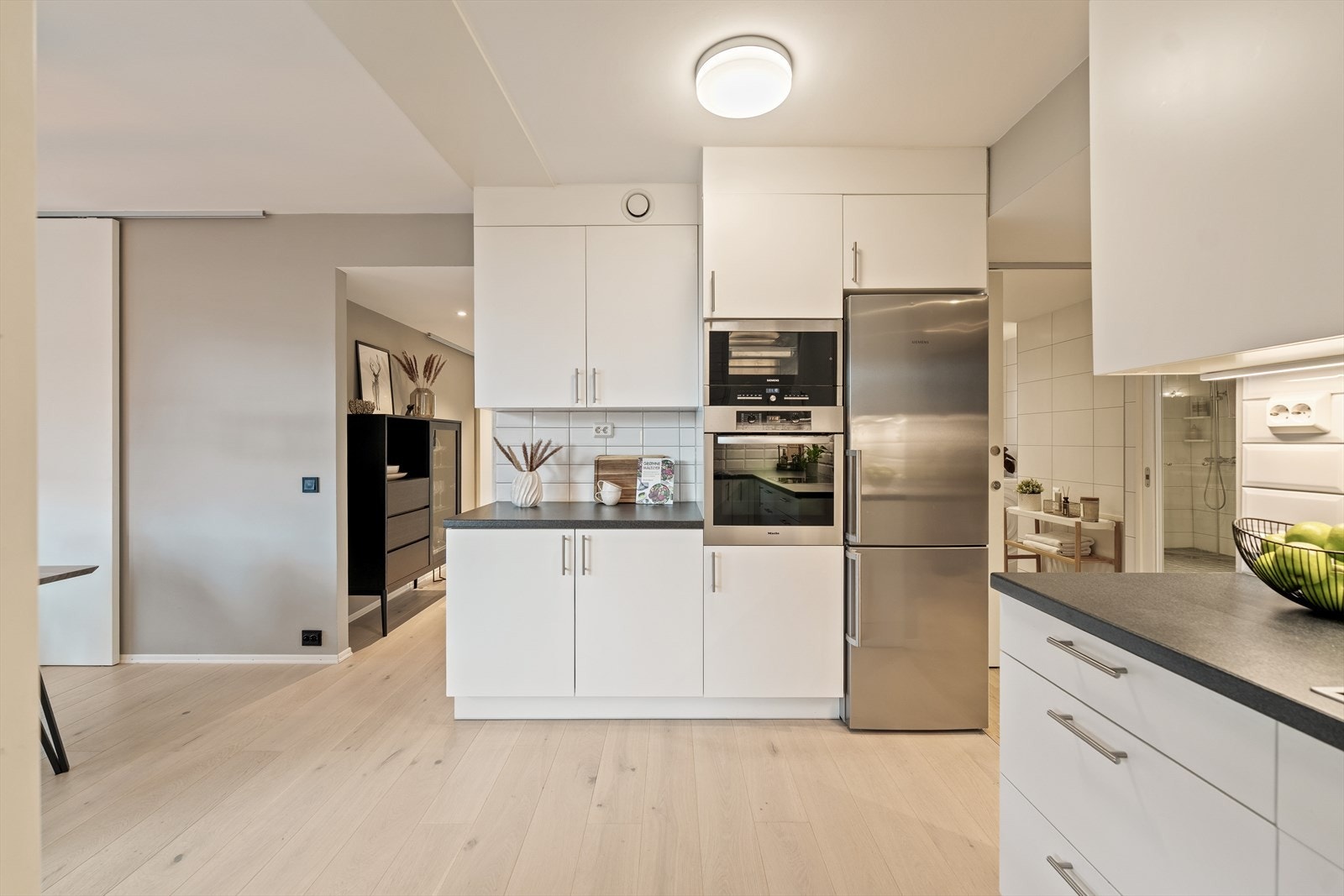 Tidløs kjøkkeninnredning med slette fronter og laminat benkeplate. Det er integrerte hvitevarer som induksjonstopp, stekeovn og dampovn. Ellers frittstående kjøl/frys og oppvaskmaskin. Galleribilde