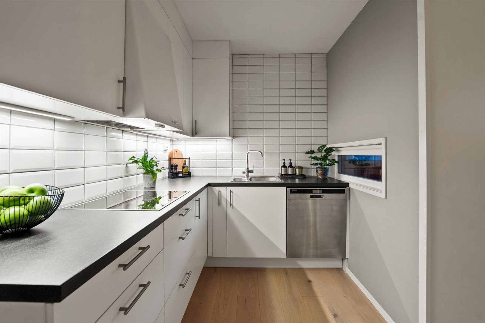 Videre har kjøkkenet nedfelt oppvaskkum med ett-greps armatur, fliser på vegg over kjøkkenbenk og benkeskapsbelysning og stikkontakter over benkeplate. Galleribilde