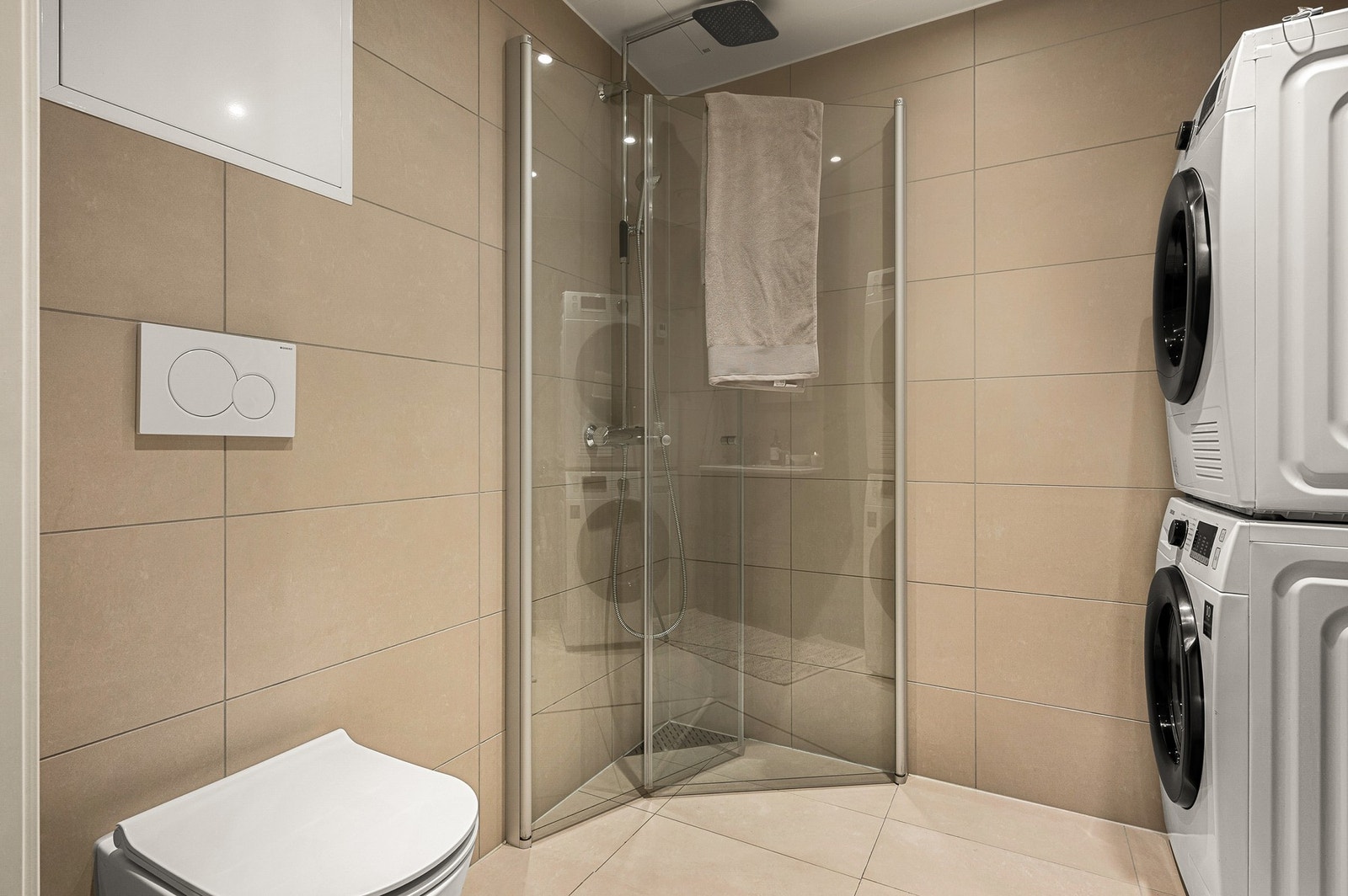 Badet har flislagte flater, dusjhjørne med innfellbare glassdører, servant med speil, samt vegghengt toalett. Galleribilde