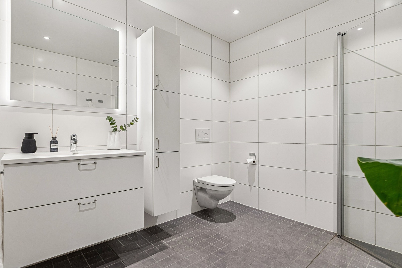 Badet er utstyrt med vegghengt toalett, dusjhjørne i glass og servantinnredning med speil. Galleribilde