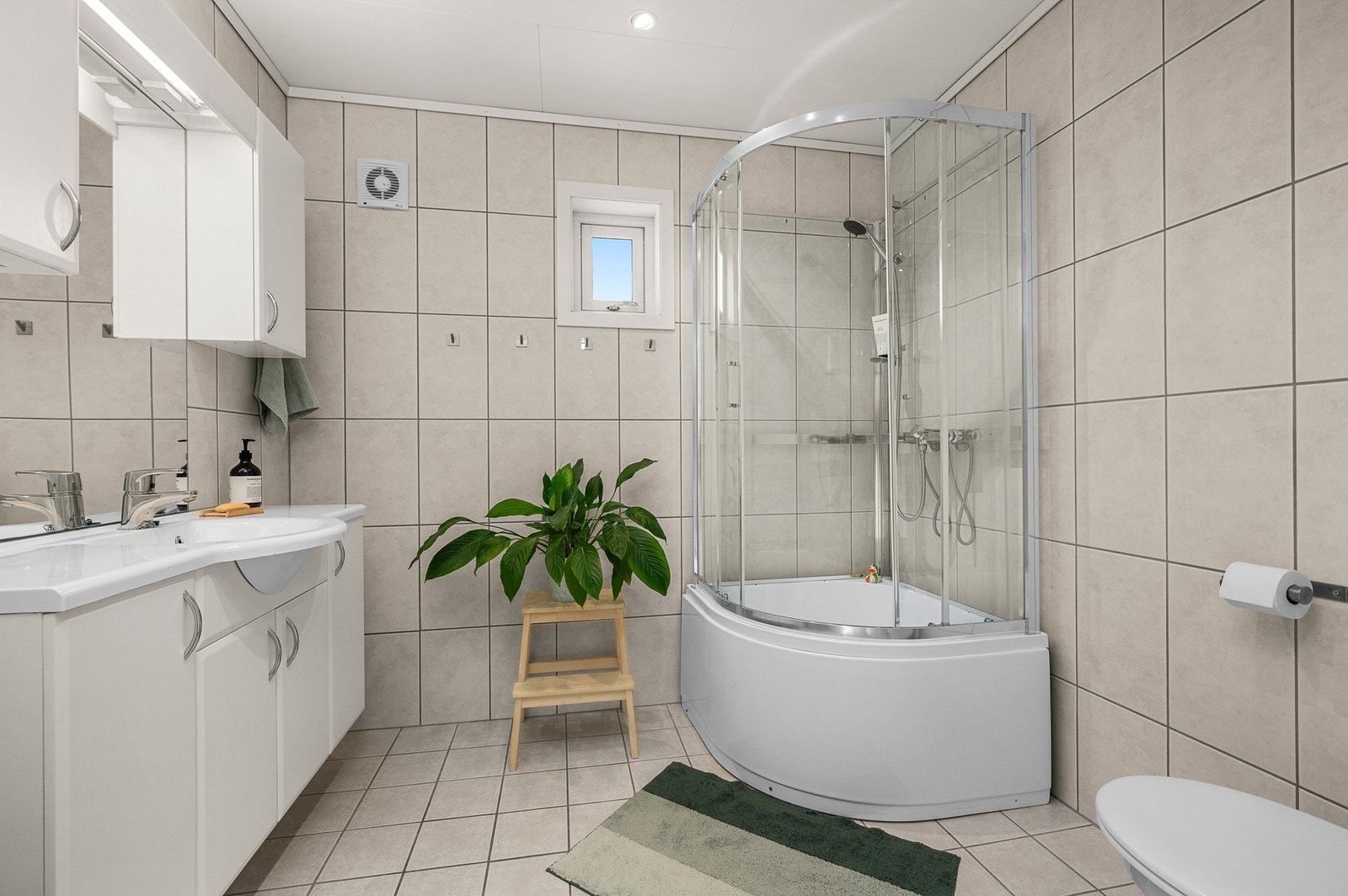 Badet er ca 5,5m2 med fliser og innredning i et nøytralt uttrykk - dusjkabinettet er skiftet i senere år, og har badekar i bunn. Galleribilde