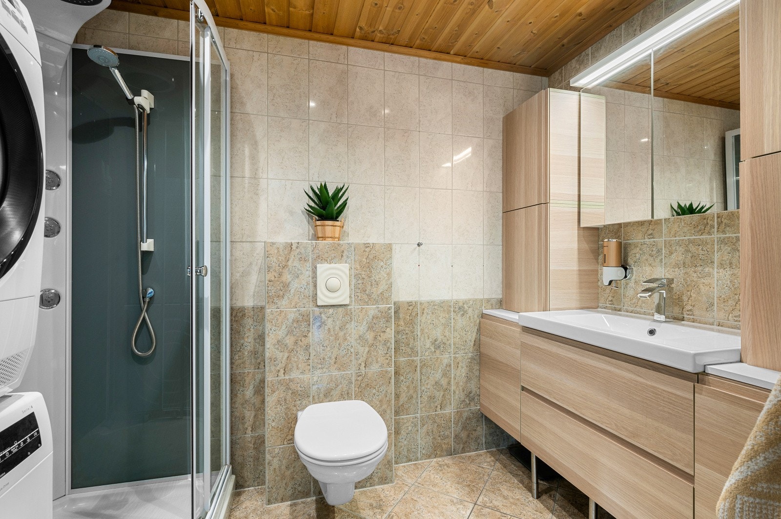 Leiligheten har et flislagt baderom innredet med veggmontert WC, nyere baderomsinnredning, dusjkabinett, og opplegg til vaskemaskin. Galleribilde