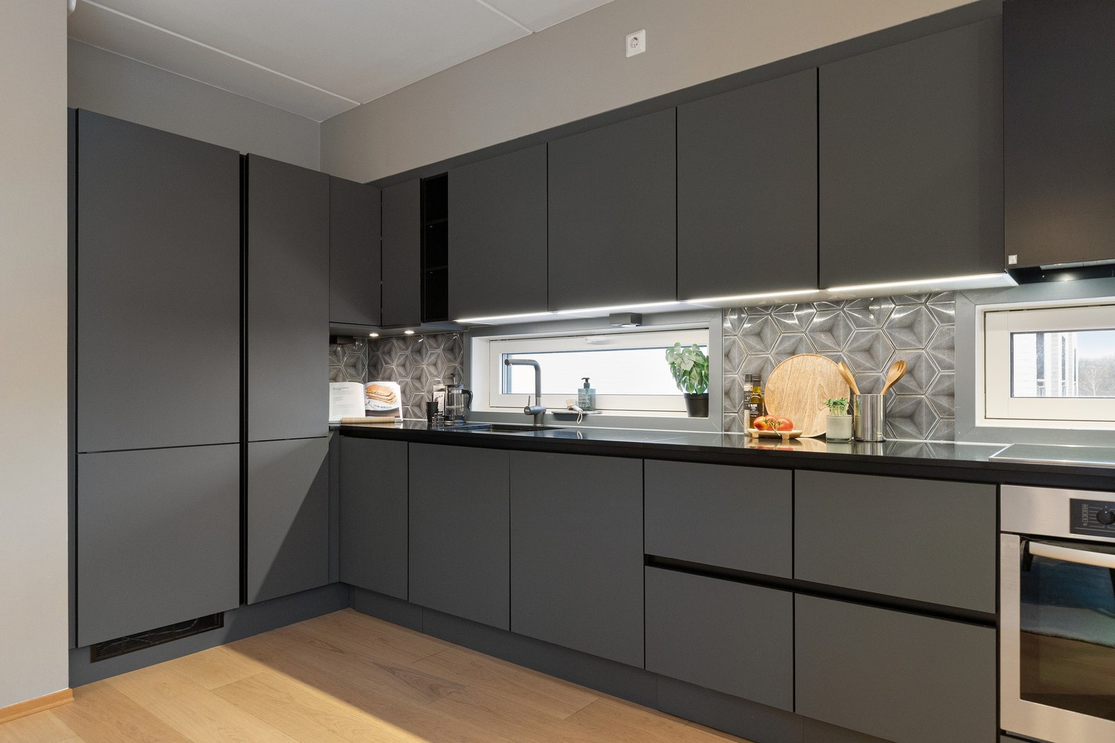 Vinduer over benkeplaten gir behagelig lysinnslipp og bidrar til et lyst og funksjonelt kjøkken med et gjennomgående tidsriktig uttrykk. Galleribilde