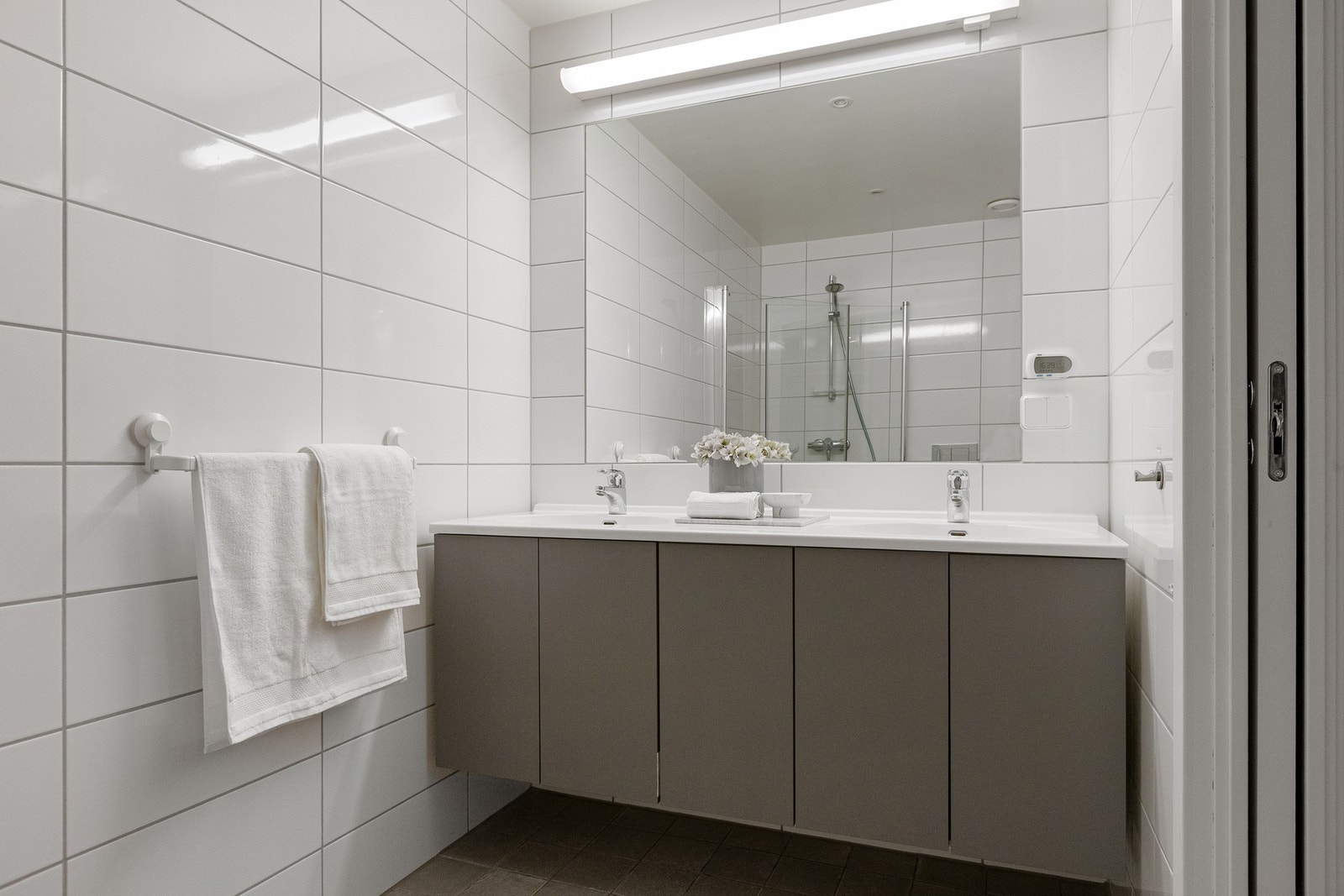 Badet er innredet med baderomsinnredning med to nedfelte servanter, veggmontert toalett samt dusjløsning med dusjvegger i hjørne. Galleribilde