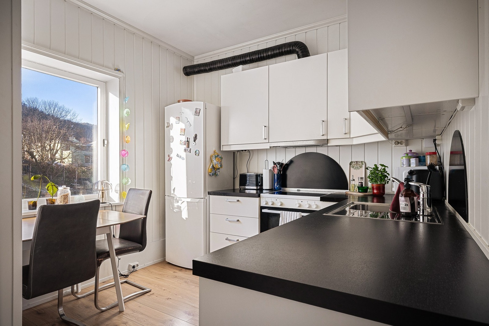 - Kjøkkenet fra 2014 har slette, hvite fronter og laminert benkeplate, og er dels åpent mot stuen - Galleribilde