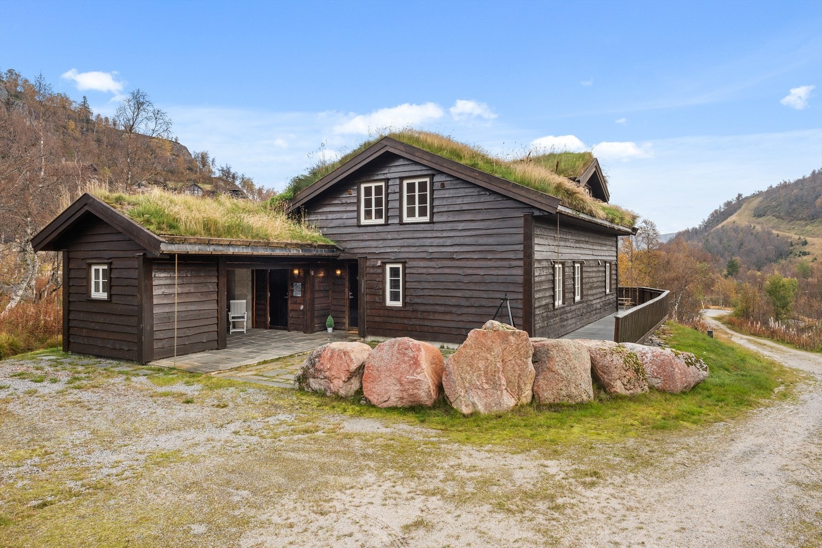 Innbydende inngangsparti med flere uteboder med overbygg mellom dem - hellelagt terrasse som flukter med terrassen rundt hytten Galleribilde