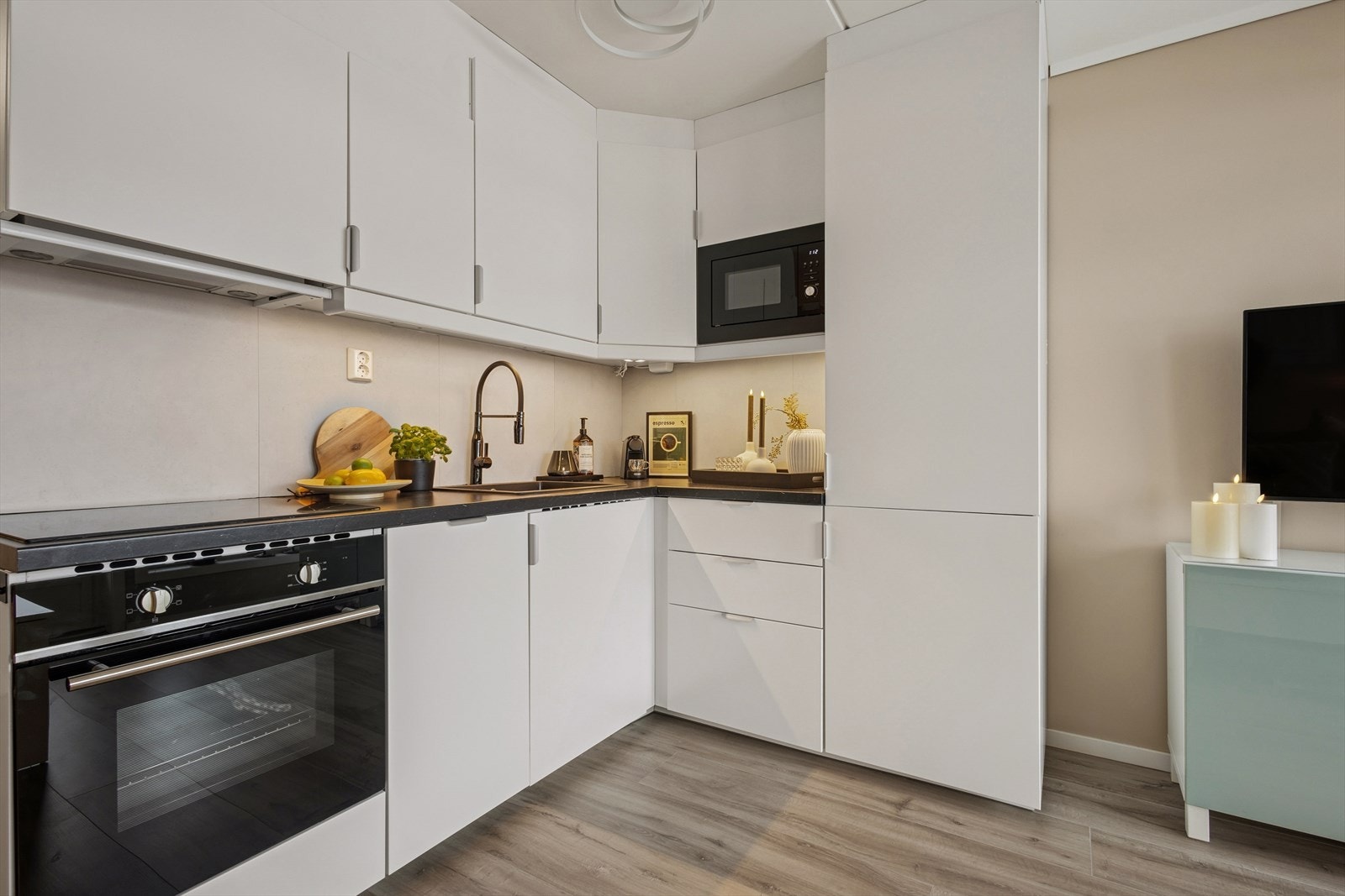 Kjøkkenet har en pen innredning med hvite, glatte fronter og laminert benkeplate med nedfelt kjøkkenkum. Galleribilde