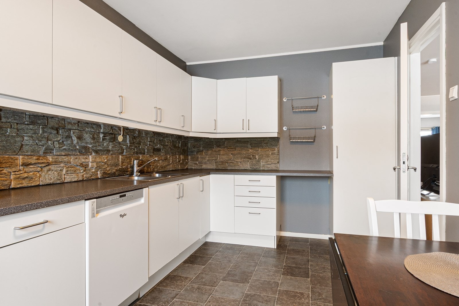 Kjøkkenet har slette hvite fronter og stilige gråstein fliser mellom benkeplaten og overskapet. Galleribilde