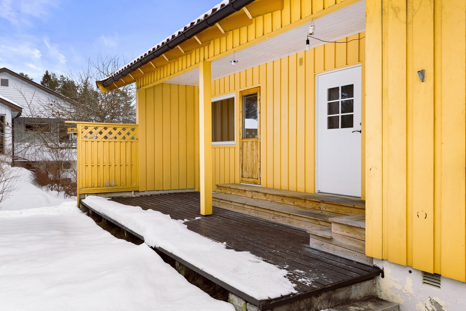 Overbygd terrasse med tregulv gir en skjermet uteplass med enkel tilgang fra kjøkkenet. Galleribilde