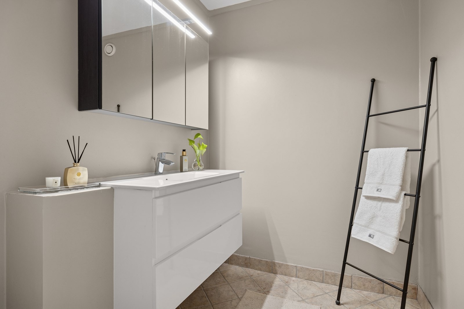 Badet har flislagt gulv og et moderne uttrykk med stort servantskap og speilskap - en stilren og funksjonell løsning Galleribilde