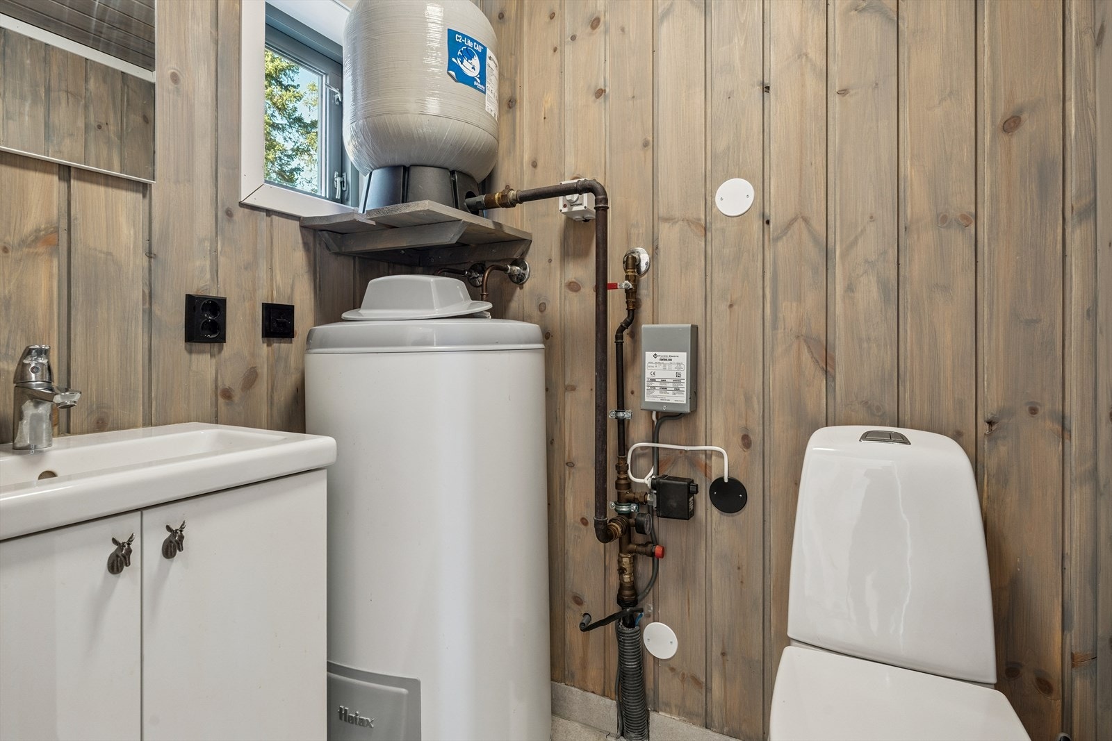 Toalettrommet har flislagt gulv med varme, servantskap og gulvmontert toalett. Her står også varmtvannsbereder og trykktank. Galleribilde