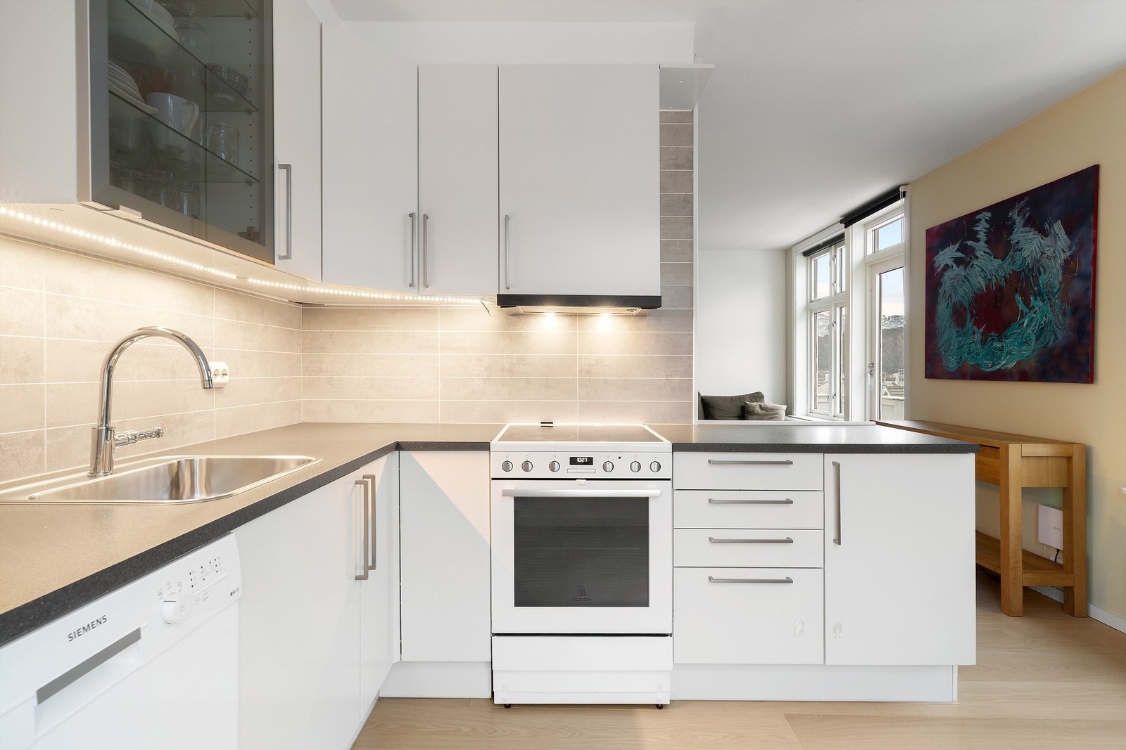 Kjøkkenet har frittstående komfyr, oppvaskmaskin og kjøleskap med fryser. Ventilator i overskap. Laminert plate mellom kjøkkenbenk og overskap Galleribilde