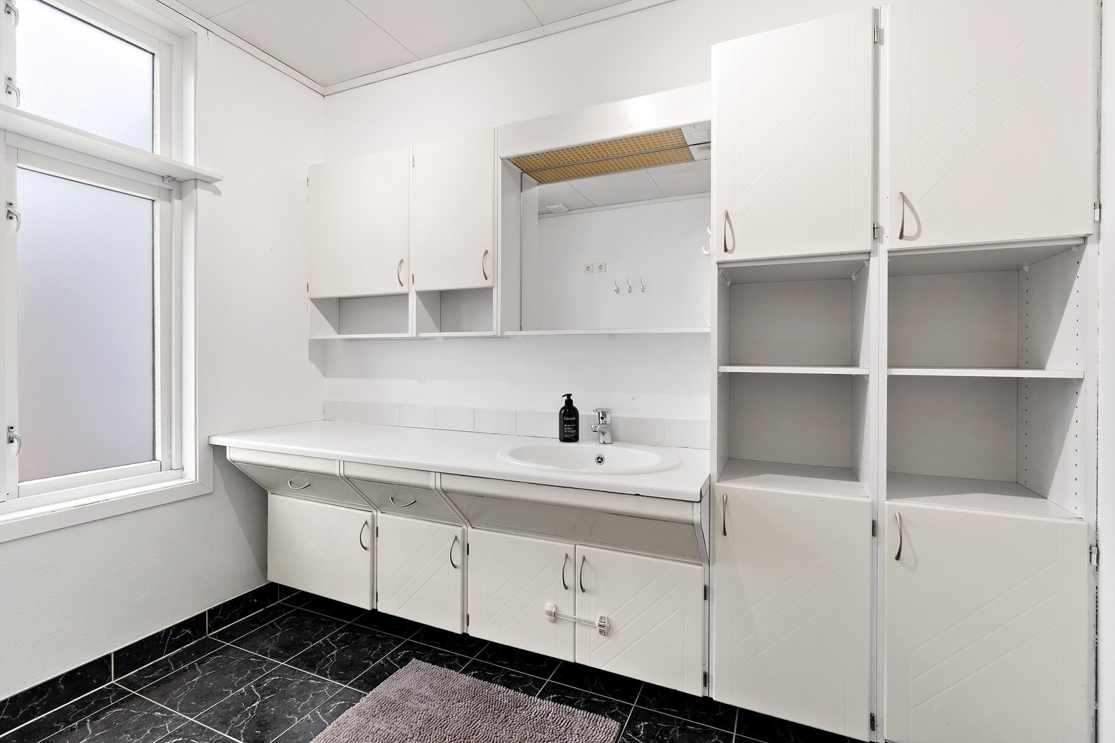 Romslig baderomsinnredning med god skapplass. Ovenpåliggende servant med ett-greps armatur. Speil med overlys og stikkontakt over servant. Galleribilde