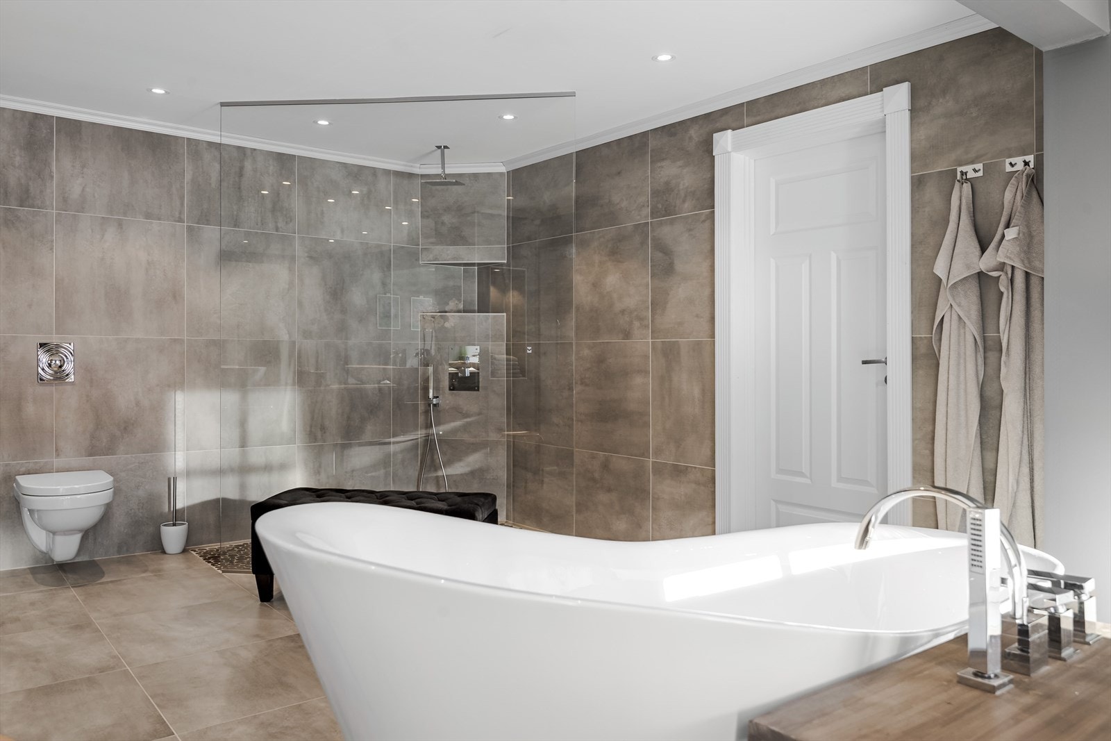 Baderommet har store flotte fliser på gulv og vegger, elektriske varmekabler i gulv, downlights i himlingen og elektrisk styrt vifte. Galleribilde