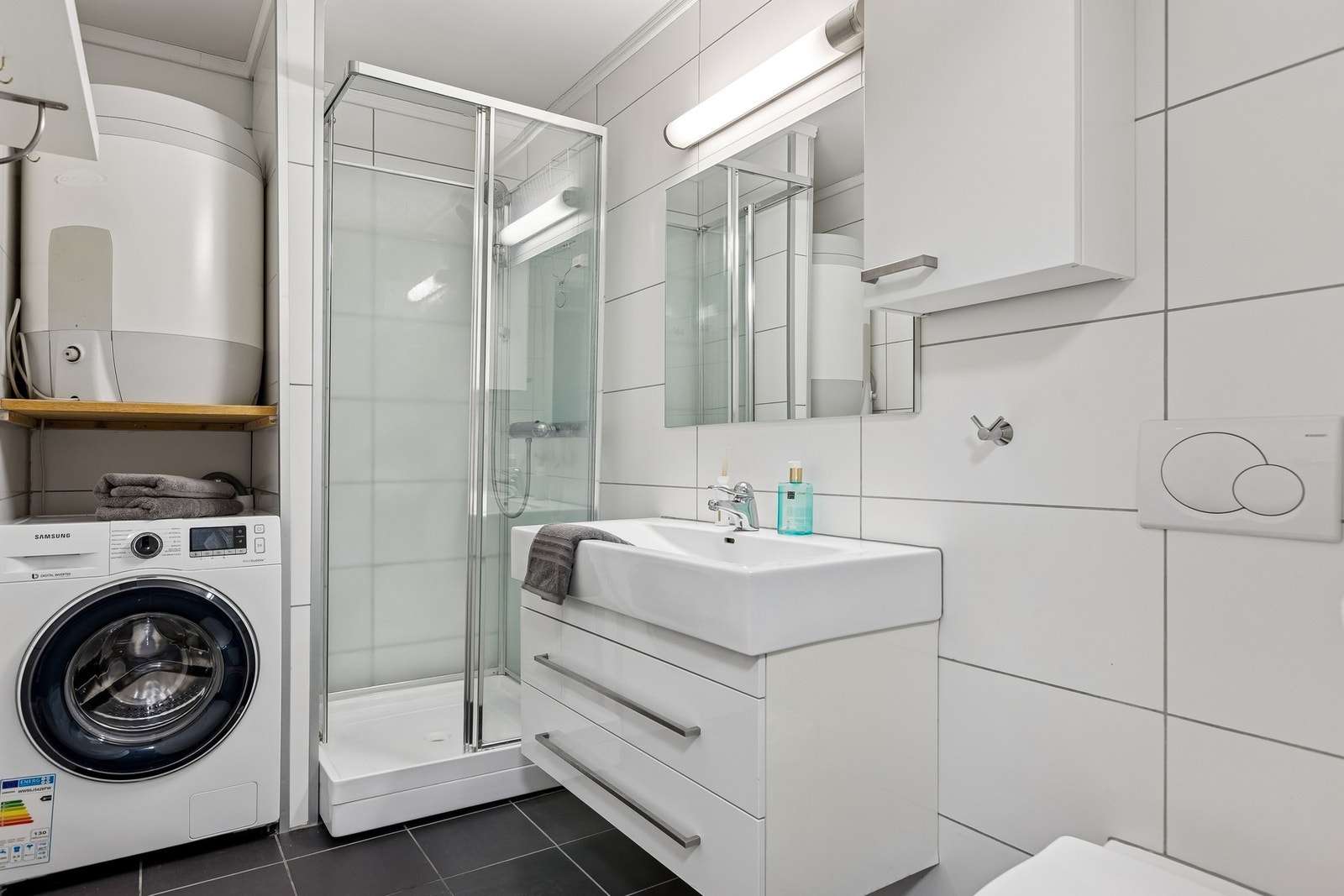 Badet er utstyrt med vegghengt servantinnredning, speil med overlys, vegghengt skap, vegghengt toalett og dusjkabinett. Galleribilde