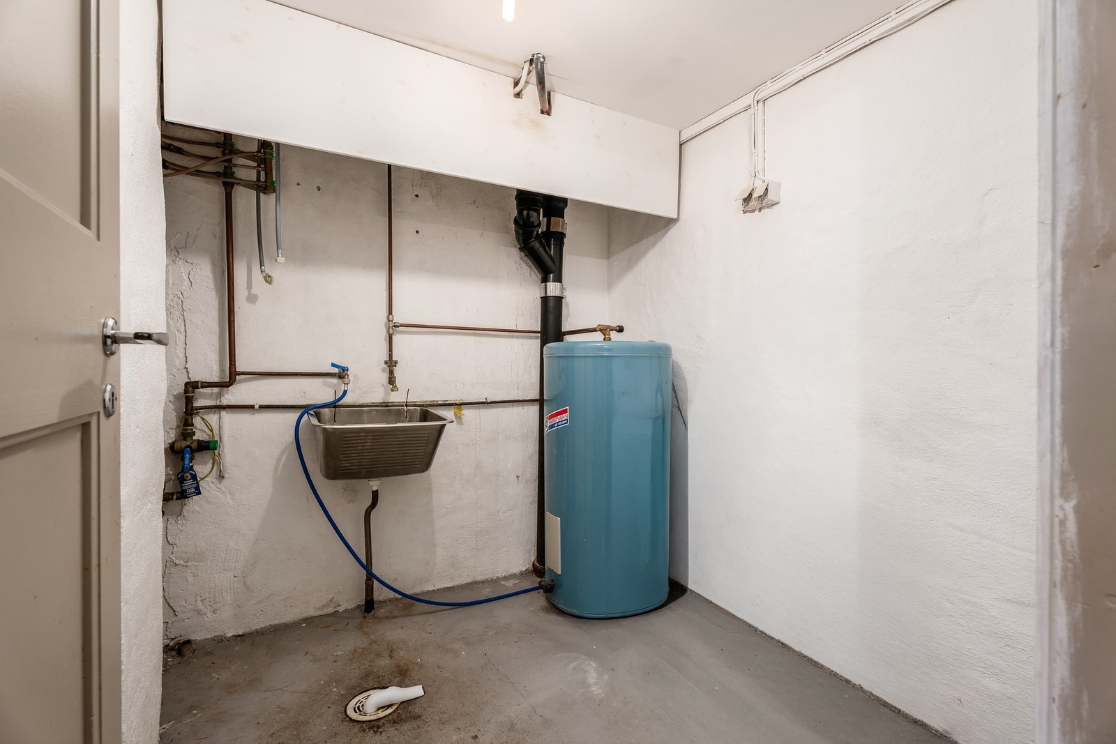 Vaskekjeller av eldre dato med gulv av betong, varmvannstank og opplegg for vaskemaskin. Galleribilde