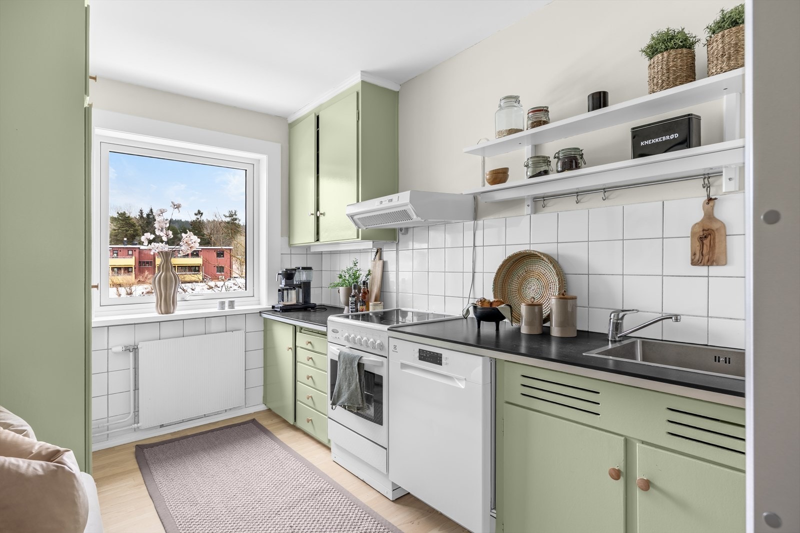 Kjøkkeninnredningen har glatte fronter, fliser på vegg over benkeskap og laminat benkeplate med kum i rustfritt stål. Galleribilde