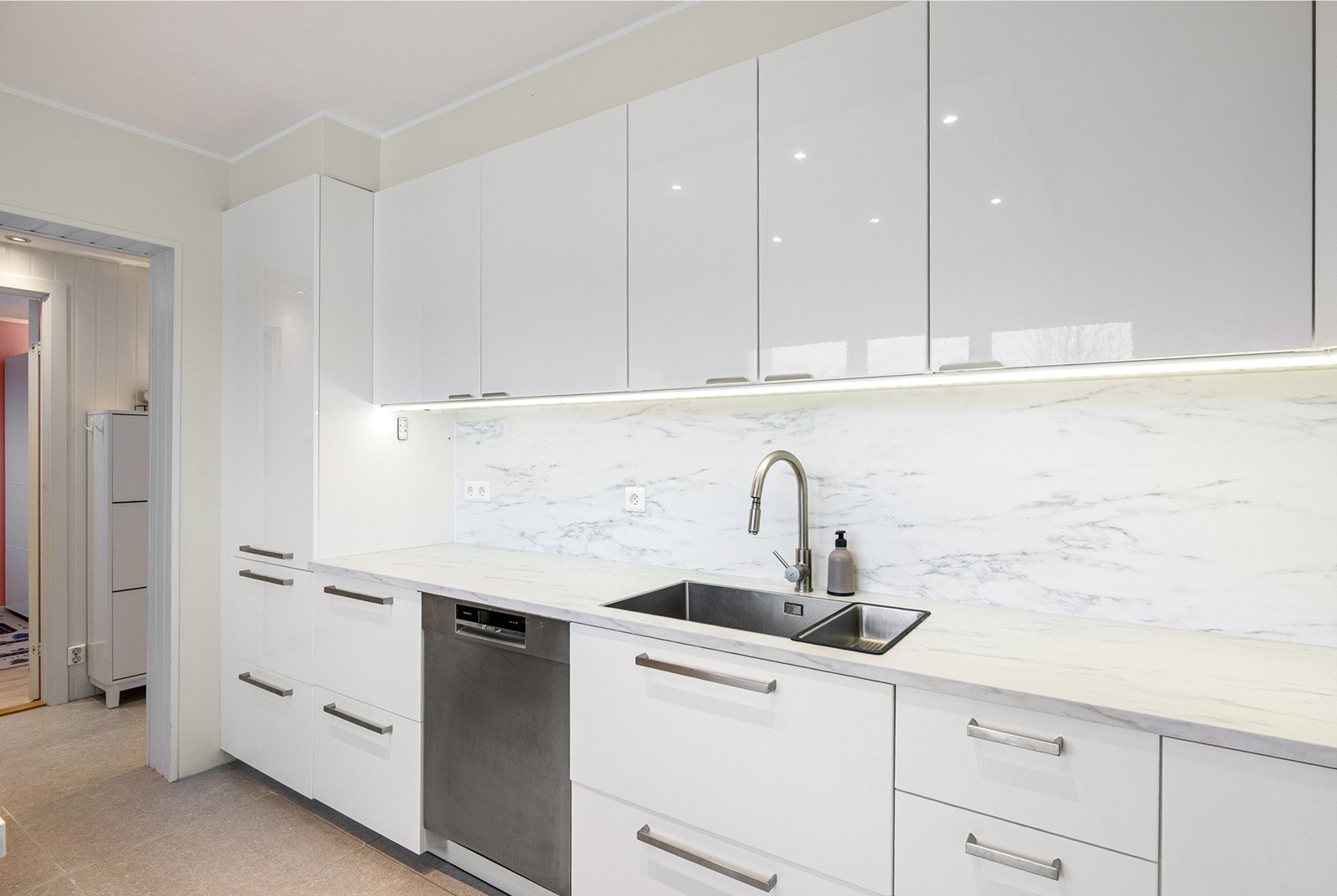 Lys kjøkkeninnredning med laminert benkeplate med nedfelt oppvaskkum med 1-greps blandebatteri. Det er opplegg for oppvaskmaskin, integrert komfyr og mikrobølgeovn samt nedfelt platetopp og det er tilkoblet en ventilator over kokeplass. Galleribilde