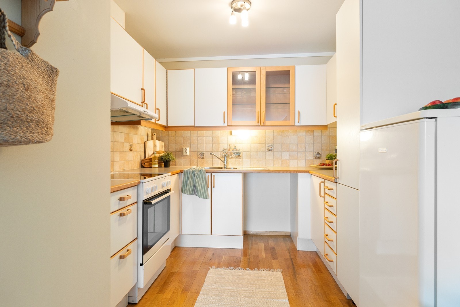 Kjøkkeninnredningen har hvite, glatte fronter, laminert benkeplate og flislagt overflater på vegg mellom overskap og benkeplaten. Galleribilde