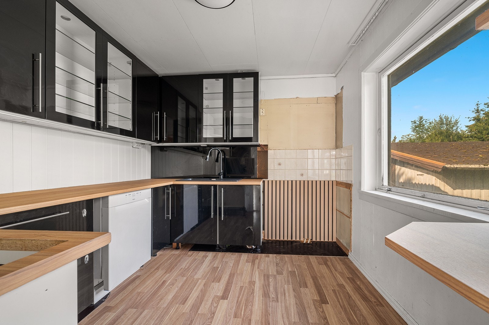 Her er avtrekk til komfyr ført ut i yttervegg. Benkeplate i laminat med benkebeslag i stål. Fliser mellom over og underskap. Galleribilde