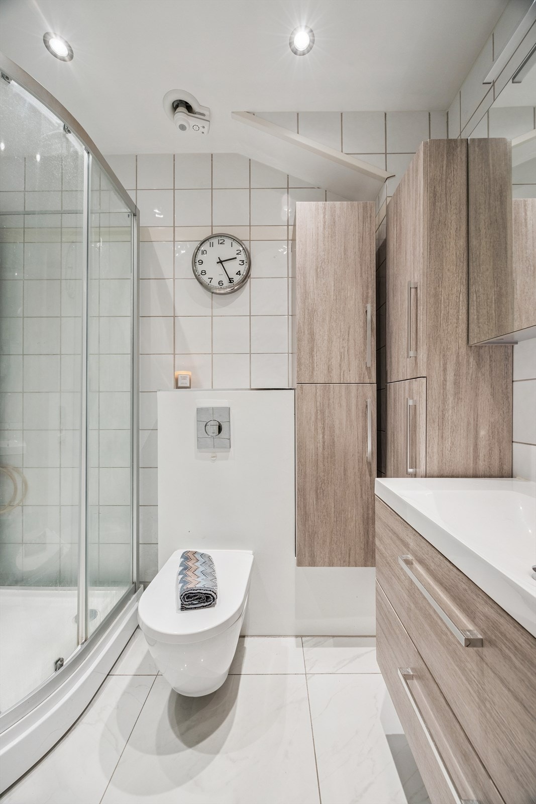 Bad med med nedfelt servant, veggmontert toalett, dusjkabinett og flislagt gulv med elektriske varmekabler. Oppgradert i 2023. Galleribilde