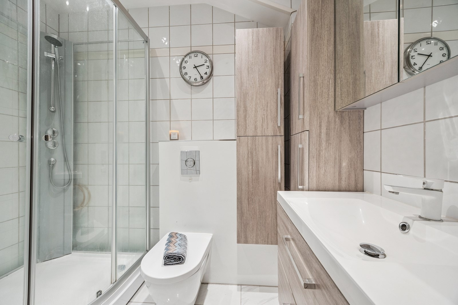 Bad med med nedfelt servant, veggmontert toalett, dusjkabinett og flislagt gulv med elektriske varmekabler. Oppgradert i 2023. Galleribilde