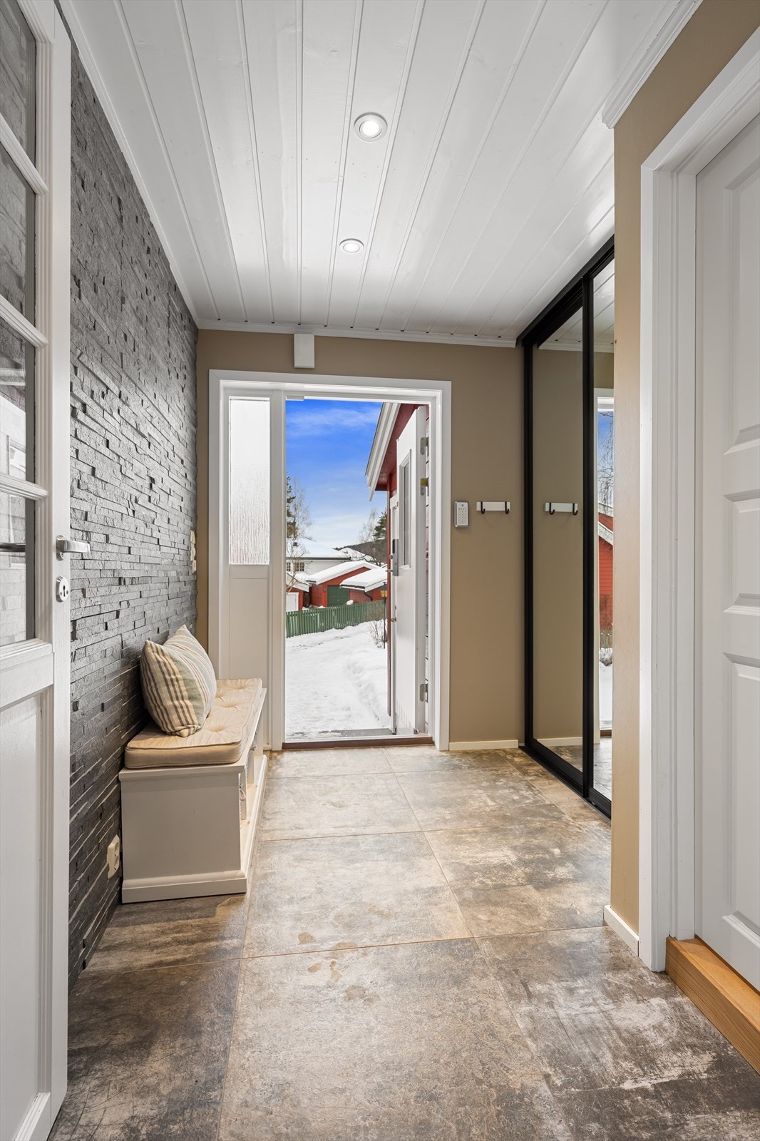 Velkommen inn i en lys entré med fliser fra 2021 med varmekabler og en dekorativ skifervegg samt en skyvedørsgarderobe. Galleribilde