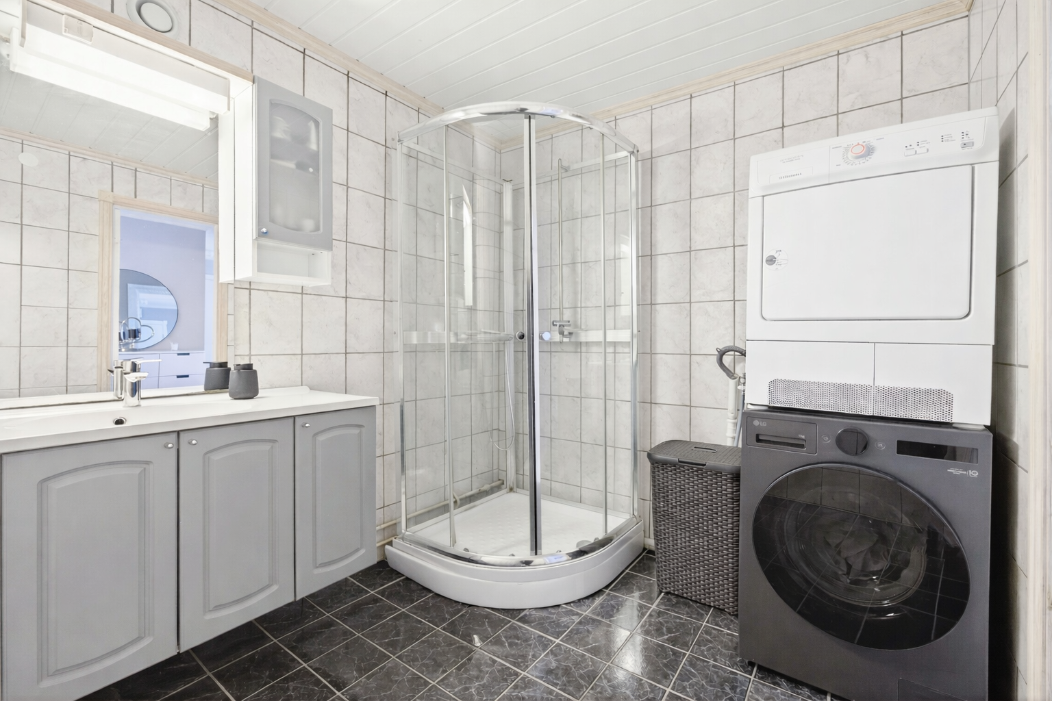 Flislagt og romslig bad med god skapplass og praktisk opplegg for vaskemaskin og tørketrommel. Et funksjonelt og ryddig bad med god plass til hverdagen. Galleribilde