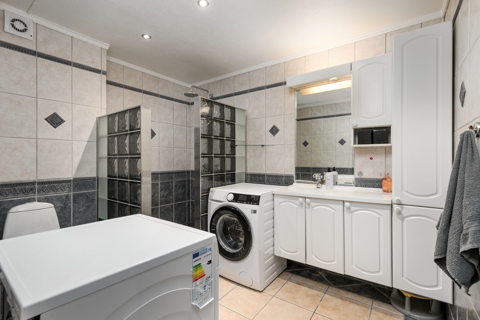 Det er separat dusjhjørne med vegger i glassbyggerstein, samt elektrisk avtrekksvifte på vegg. Badet har opplegg og plass til vaskemaskin og tørketrommel. Galleribilde