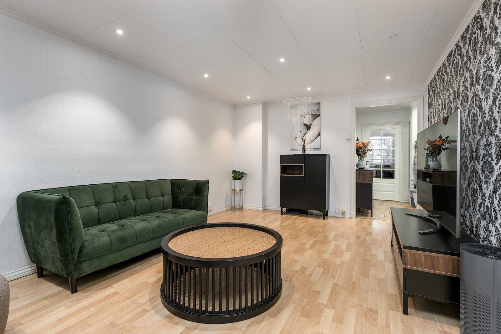 Den åpne stuen fremstår som tiltalende med lysmalte vegger og en kontrastvegg med tapet. Gulvet er belagt med laminat og himlingen er lyssatt med downlights. Galleribilde