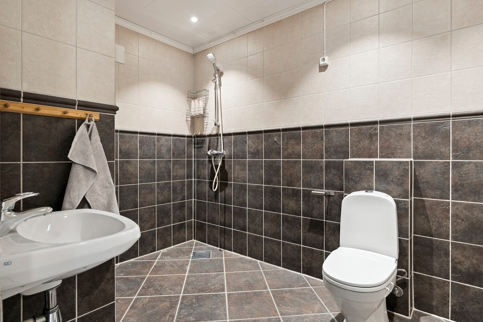 På det flislagte badet er det montert vegghengt porselenservant og skap med speil. Det er også toalett og åpen dusjløsning med forheng, samt mekanisk avtrekk via avtrekksvifte på loft. Galleribilde