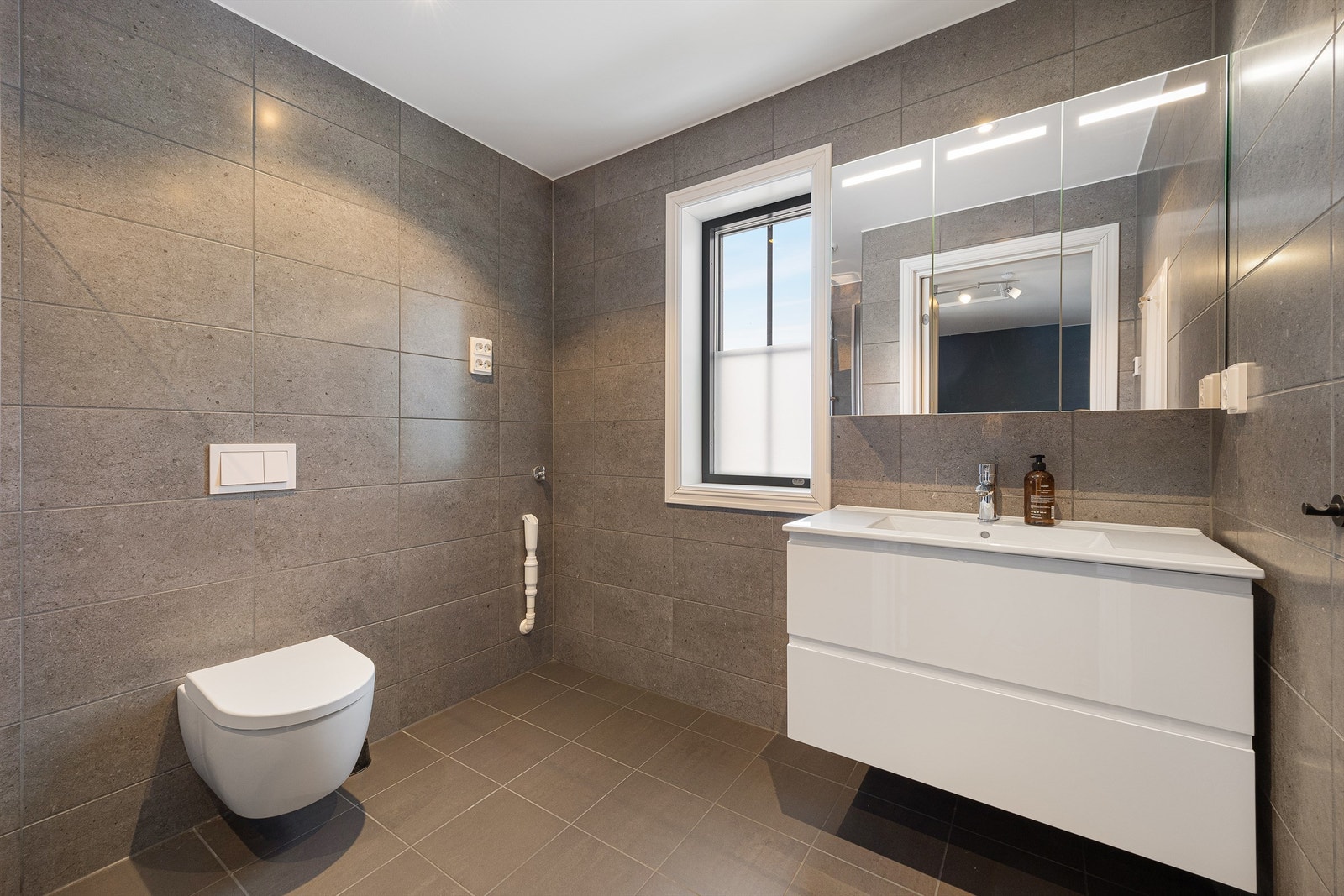 Delikat, flislagt bad med vegghengt toalett og servantinnredning med gode skuffer. Galleribilde