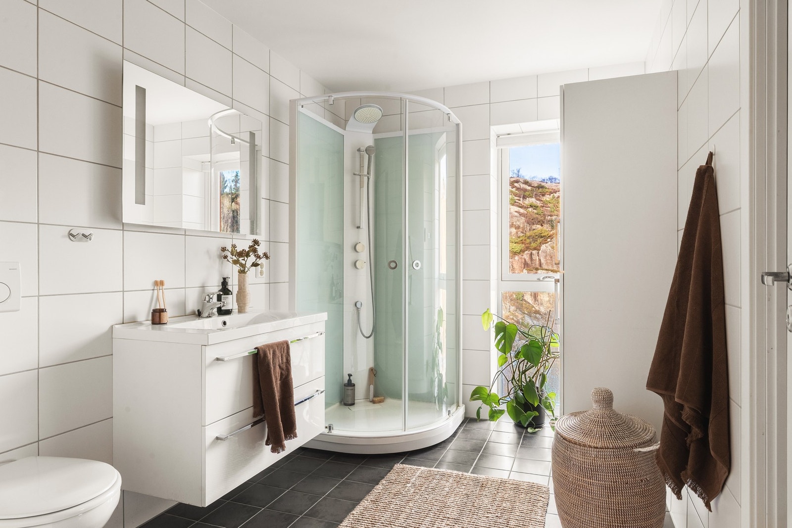 Badet er helfliset og holder en moderne standard. Her er det varmekabler i gulvet, vegghengt toalett, dusjkabinett, baderomsinnredning og speil med integrert belysning. Galleribilde