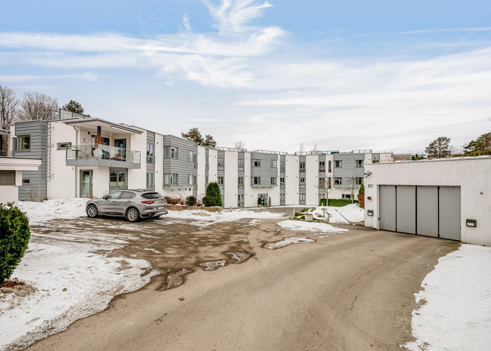Asfaltert innkjørsel, omkranset av grøntområder. Gjesteparkeringsplasser og adkomst til lukket garasjeanlegg Galleribilde