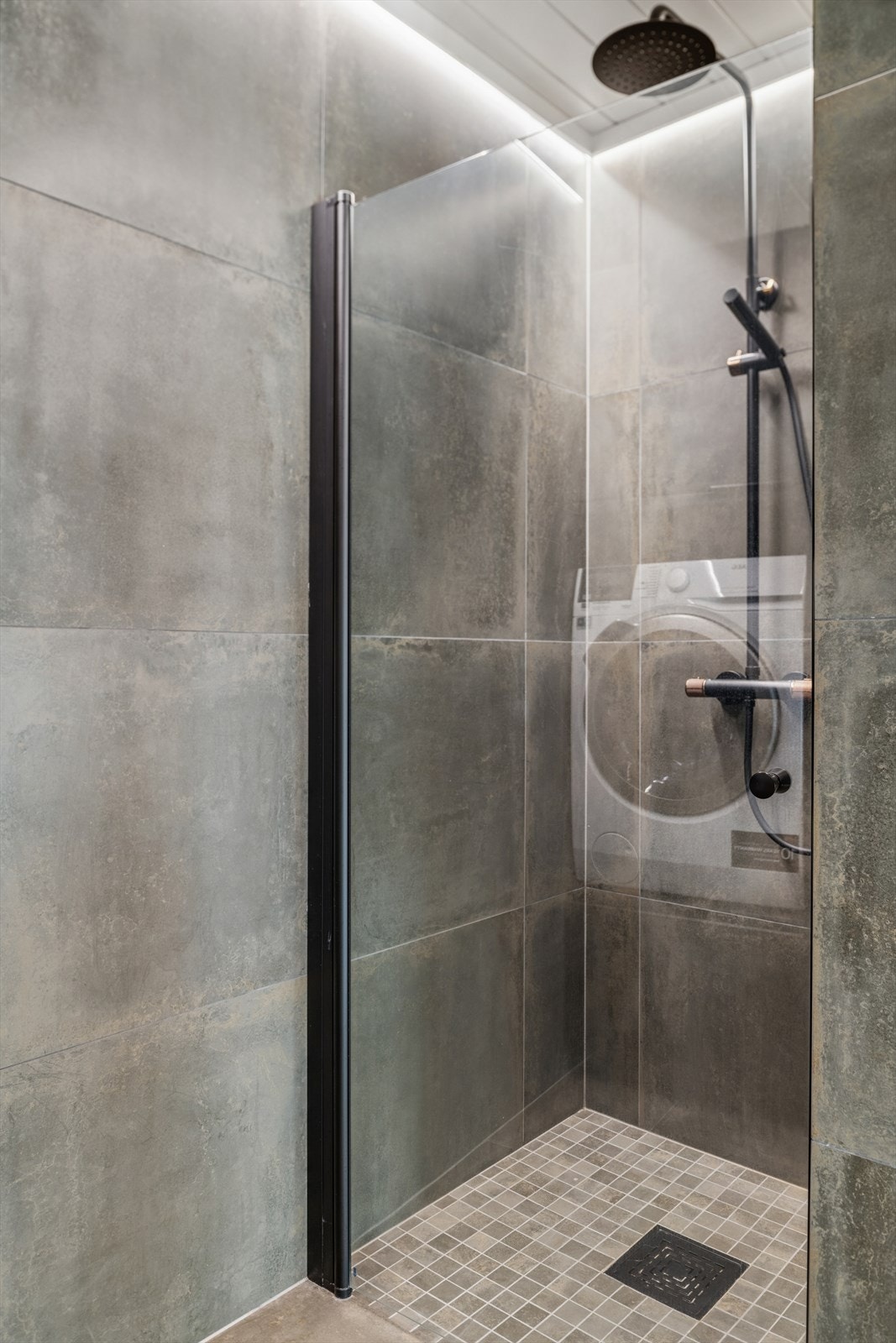 Dusjnisje med glassdør og flislagte overflater på gulv og vegger. Nisjen er etablert av en del av opprinnelig bod. Ukjent om det er søkt bruksendring og godkjent. Galleribilde