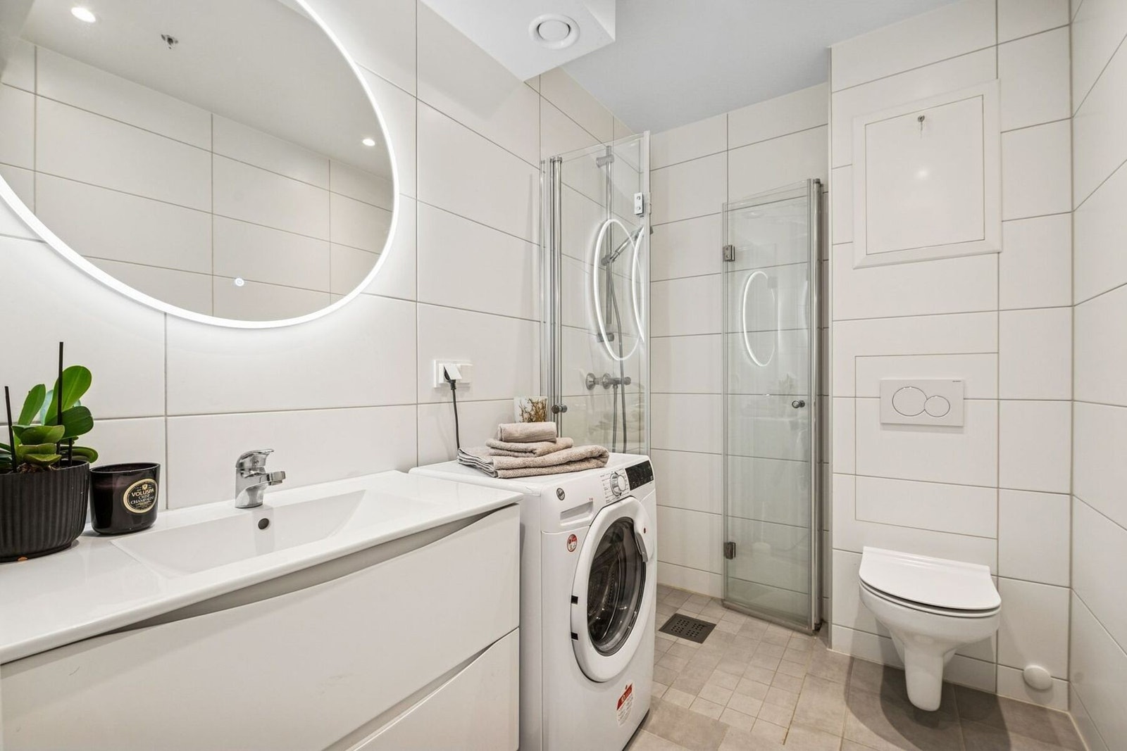 Delikat og moderne bad med dusjhjørne, vegghengt toalett og opplegg for vaskemaskin. Galleribilde