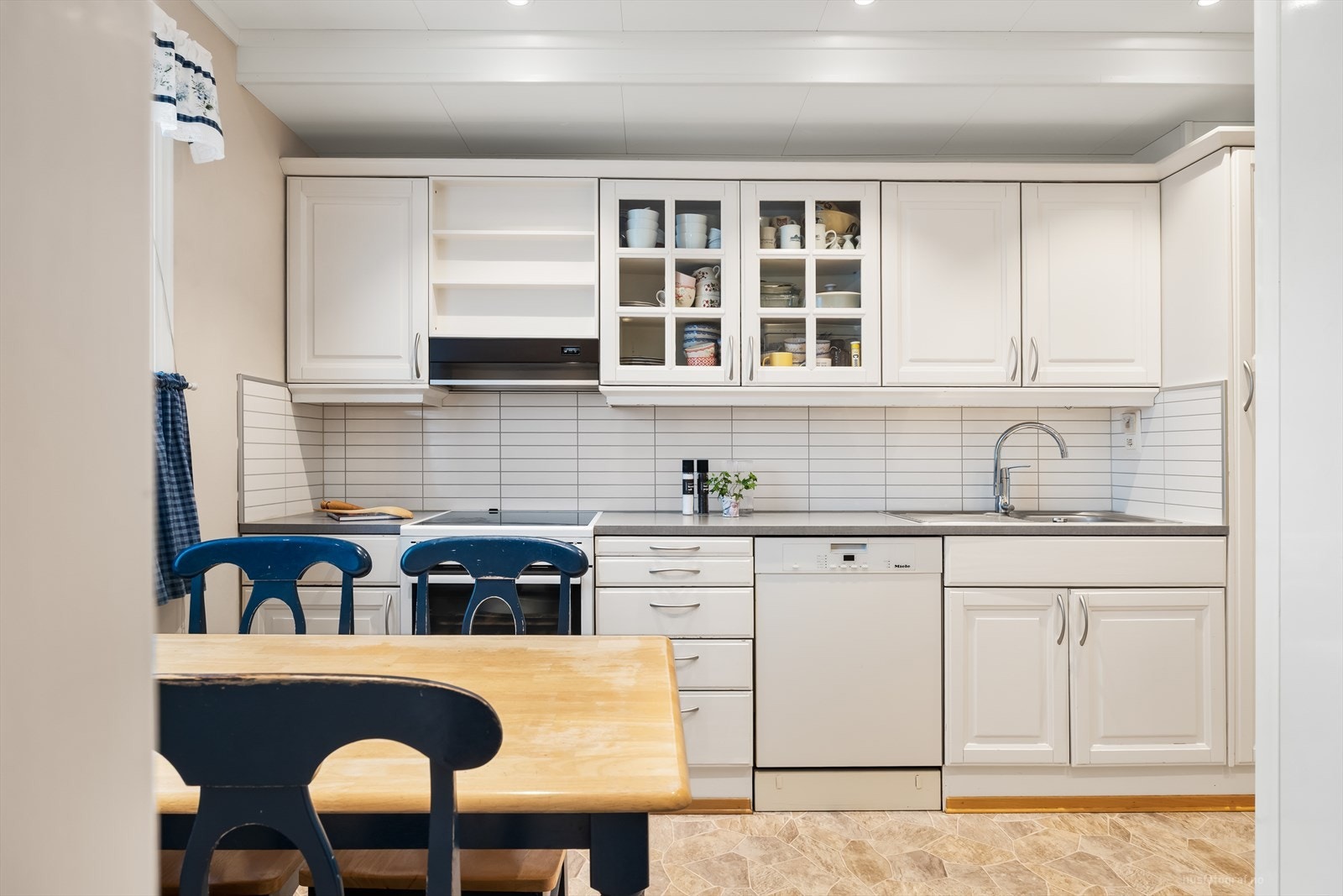 Klassisk kjøkkeninnredning med behandlet innredning med profilerte hvite fronter og benkeplate av laminat. Galleribilde