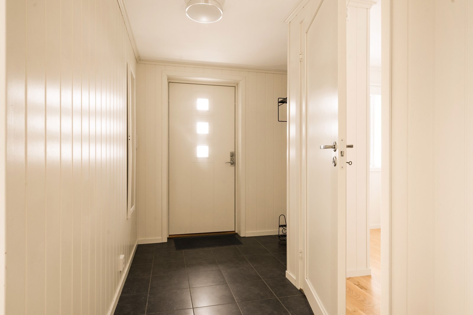 Lysmalt entré med flislagt gulv og gulvvarme. Nisje hvor det er montert knaggrekke. Galleribilde